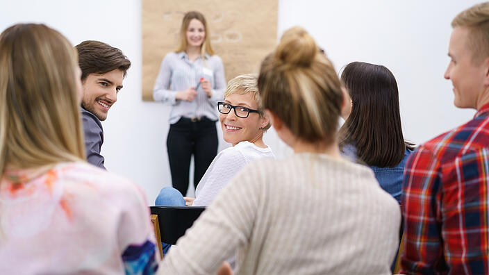 Seminarsituation: eine Frau dreht sich aus vorderer Reihe um und schaut lächelnd nach hinten.