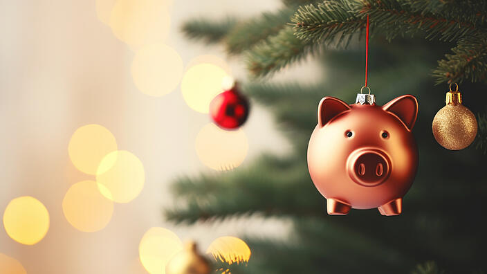 Ein Sparschwein hängt wie eine Weihnachtskugel am Tannenbaum