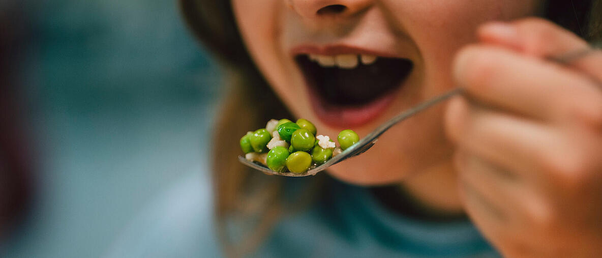 Ein Mädchen isst in der Schulkantine / Gabel mit Reis und Erbsen   
