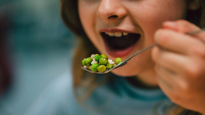 Ein Mädchen isst in der Schulkantine / Gabel mit Reis und Erbsen   