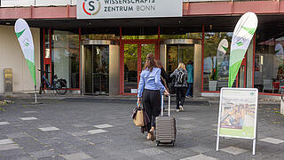 Eine Veranstaltungsteilnehmerin läuft mit Rollkoffer ins Wissenschaftszentrum Bonn