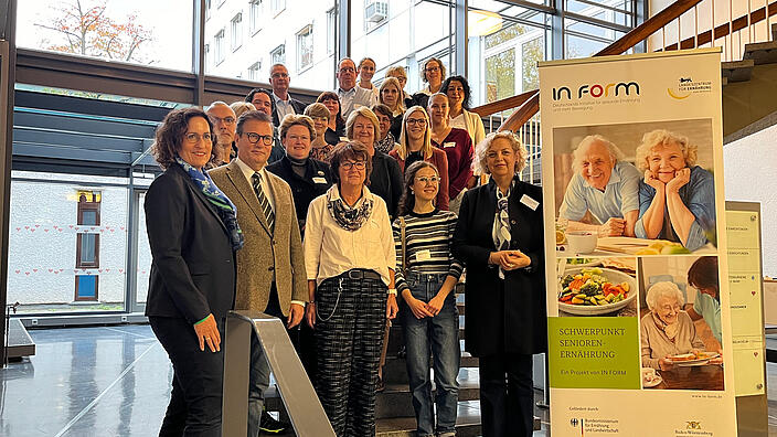 Dr. Kiran Virmani mit Vertreterinnen und Vertretern der zertifizierten Einrichtungen auf einer Treppe stehend mit einem Banner von IN FORM
