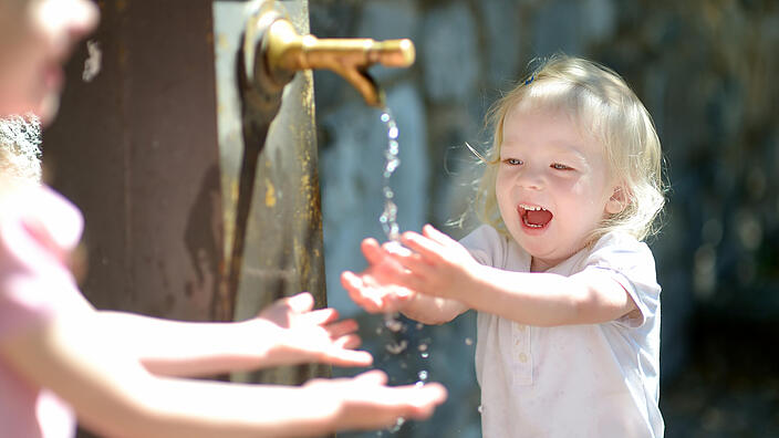 Kleine Mädchen spielen am Brunnen mit Wasser.