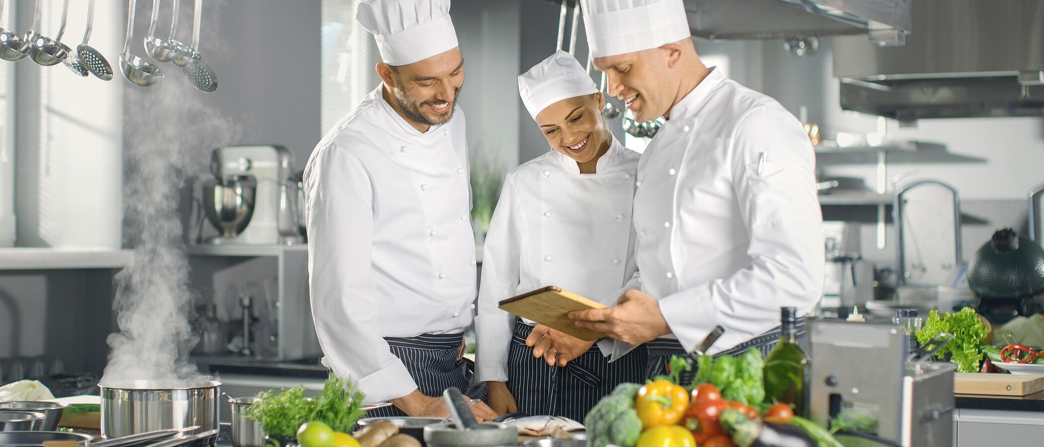 3 Köche stehen in einer Küche und planen Essen an einem Tablet