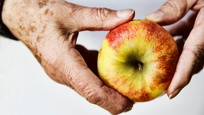 ein älterer Mensch hält einen Apfel mit zwei Händen