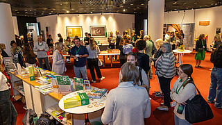Personen stehen im Foyer an den Tischen und trinken Kaffee oder Tee