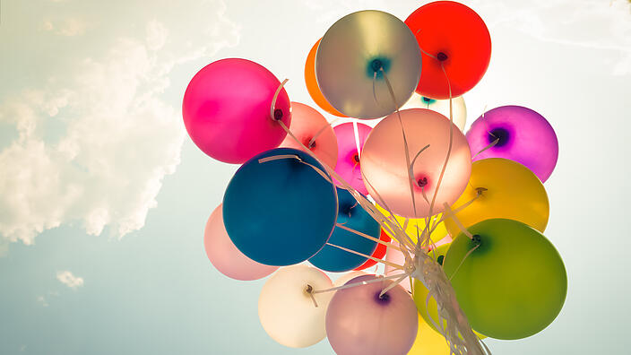 mehrere zusammengeknotete Luftballons fliegen in den Himmel