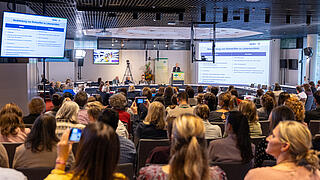 Dr. Ralf Greiner steht am Rednerpult, im Vordergrund befinden sich die Zuhörer*innen