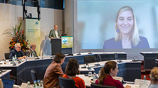 Herr Prof. Dr. Sascha Rohn steht am Pult auf der Videoleinwand sieht man Frau Dr. Mathilde Touvier dazugeschaltet.