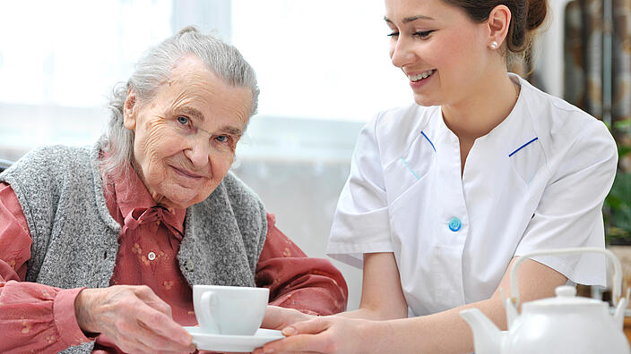 Junge Frau reicht einer Seniorin eine Tasse.