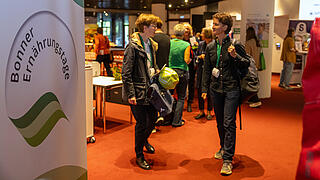 Zwei Personen unterhalten sich lebhaft. Links daneben ein Banner mit der Aufschrift „Bonner Ernährungstage“